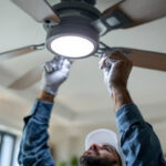 A photograph of a skilled lighting contractor installing or adjusting a ceiling fan switch in a well-lit room