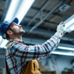 A photograph of a lighting contractor installing or inspecting fluorescent lights in a commercial or residential setting