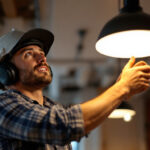 A photograph of a skilled lighting contractor installing or adjusting a stylish commercial hanging light in a modern