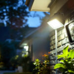 A photograph of a lighting contractor installing motion sensor flood lights in a residential setting