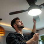 A photograph of a skilled lighting contractor installing a stylish ceiling fan with integrated lighting in a modern home setting
