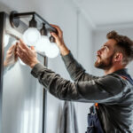 A photograph of a lighting contractor installing a stylish bathroom vanity light in a modern bathroom setting