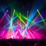 A photograph of a dynamic concert scene showcasing an array of vibrant light fixtures illuminating the stage and audience