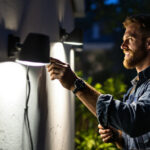 A photograph of a lighting contractor installing high-quality outdoor floodlights in a residential or commercial setting