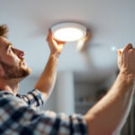 A photograph of a skilled lighting contractor installing a recessed light fixture in a modern home setting