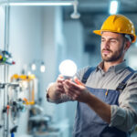 A photograph of a lighting contractor examining a modern fluorescent light bulb in a well-lit workspace