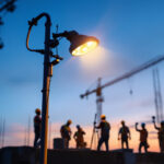 A photograph of a well-lit outdoor security lamp illuminating a construction site at dusk