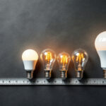 A photograph of a variety of light bulbs with different standard base sizes displayed alongside a measuring tape