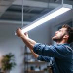 A photograph of a professional lighting contractor installing a sleek 4ft led light fixture in a modern workspace