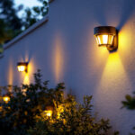 A photograph of a beautifully illuminated outdoor space featuring various styles of solar wall lights installed on a home or garden wall