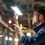 A photograph of a lighting contractor installing a sleek surface-mounted led fixture in a modern commercial space