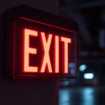 A photograph of a battery-powered exit sign illuminated in a dimly lit environment