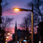 A photograph of a beautifully illuminated modern lamp post in an urban setting during twilight