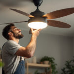 A photograph of a lighting contractor installing a stylish light fitting on a ceiling fan in a modern home setting