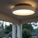A photograph of a stylish outdoor flush mount ceiling light installed in a beautifully landscaped patio or porch setting