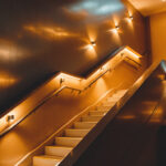 A photograph of a well-lit stairwell featuring modern lighting fixtures that highlight the architectural details and create a warm