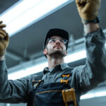 A photograph of a lighting contractor inspecting or installing 4-foot fluorescent lamps in a commercial or industrial setting