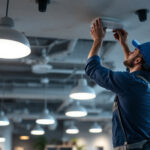 A photograph of a well-lit workspace featuring a lighting contractor installing led high hats in a modern ceiling