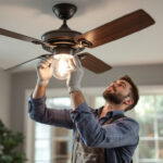 A photograph of a lighting contractor installing a stylish fan light fixture in a modern home setting
