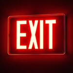 A photograph of a glowing exit sign in a dimly lit environment