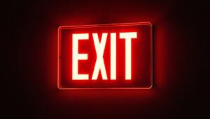 A photograph of a glowing exit sign in a dimly lit environment