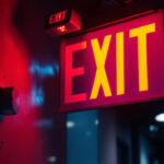 A photograph of a well-lit exit sign equipped with emergency lights in a commercial or public building setting