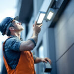 A photograph of a lighting contractor installing or inspecting a modern led wall pack light in an outdoor commercial setting