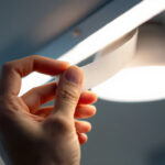 A photograph of a close-up shot of a hand applying dimming tape to a light fixture