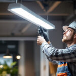 A photograph of a lighting contractor installing a 4-foot led light fixture in a commercial space