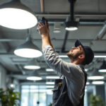 A photograph of a lighting contractor expertly installing modern suspended ceiling lighting in a commercial space