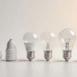 A photograph of a close-up view of various standard light bulb bases alongside a light bulb and a measuring tape