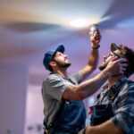 A photograph of a lighting contractor installing recessed light bulbs in a modern home setting