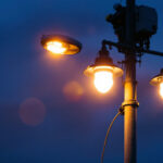 A photograph of a well-lit street pole at dusk with a lighting contractor installing or adjusting fixtures