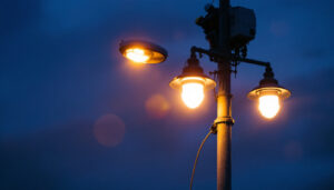 A photograph of a well-lit street pole at dusk with a lighting contractor installing or adjusting fixtures