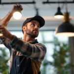 A photograph of a skilled lighting contractor installing or adjusting various types of lighting fixtures in a well-lit