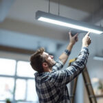 A photograph of a lighting contractor installing a modern fluorescent light fixture in a commercial space