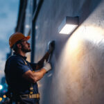A photograph of a lighting contractor installing a led wall pack with a photocell on a commercial building