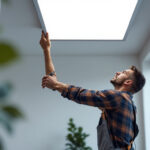 A photograph of a lighting contractor installing a sleek flat panel light in a modern space