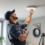 A photograph of a skilled electrician installing a recessed can light conversion kit in a modern home setting