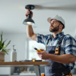 A photograph of a lighting contractor installing a ceiling light mounting bracket in a modern home setting