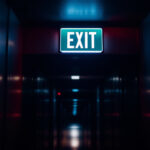A photograph of a well-lit emergency exit sign in a dimly lit corridor
