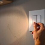 A photograph of a skilled lighting contractor installing a combination light and fan switch in a modern home setting