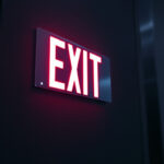 A photograph of a well-lit exit sign in a dimly lit environment