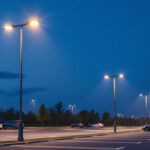 A photograph of a well-lit parking lot showcasing a row of modern light poles in action during dusk