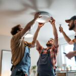 A photograph of a team of electricians or lighting professionals collaborating on the installation and adjustment of ceiling light cans in a well-lit room