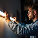 A photograph of a lighting contractor expertly installing or adjusting a wall strip light in a modern interior setting