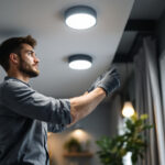 A photograph of a lighting contractor expertly installing recessed lighting cans in a modern home