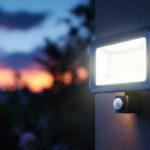 A photograph of a solar flood light with a motion sensor installed in a garden setting at dusk