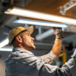 A photograph of a lighting contractor installing or adjusting a fluo lighting fixture in a modern workspace