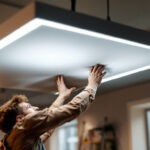 A photograph of a lighting contractor installing or adjusting flat panel led lights in a modern commercial or residential space